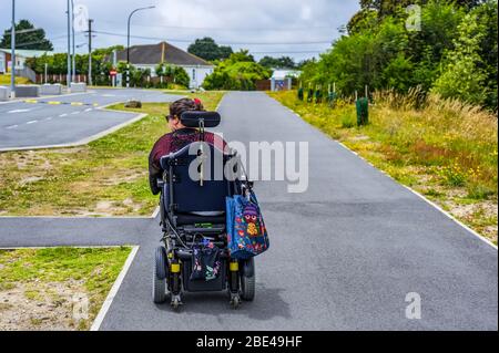 Maori-Frau mit zerebraler Palsy im Rollstuhl, die einen Bürgersteig hinuntergeht; Wellington, Neuseeland Stockfoto