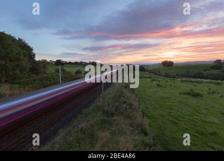 Erster TransPennine Express-Zug der Baureihe 350 auf der Hauptlinie der Westküste, die bei Sonnenuntergang mit Bewegungsunschärfe durch die Landschaft in Cumbria nach Süden fährt Stockfoto