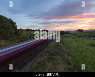 Erster TransPennine Express-Zug der Baureihe 350 auf der Hauptlinie der Westküste, die bei Sonnenuntergang mit Bewegungsunschärfe durch die Landschaft in Cumbria nach Süden fährt Stockfoto