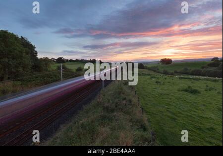 Erster TransPennine Express-Zug der Baureihe 350 auf der Hauptlinie der Westküste, die bei Sonnenuntergang mit Bewegungsunschärfe durch die Landschaft in Cumbria nach Süden fährt Stockfoto