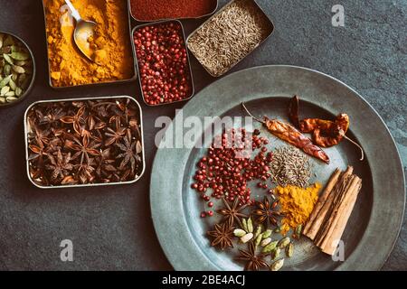 Aromatische Gewürze in Dosen auf und um einen Zinnteller auf Schiefergrund Stockfoto