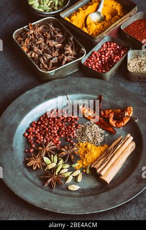 Aromatische Gewürze in Dosen auf und um einen Zinnteller auf Schiefergrund Stockfoto