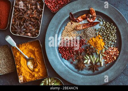 Aromatische Gewürze in Dosen auf und um einen Zinnteller auf Schiefergrund Stockfoto