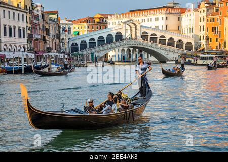 Gondeln und Gondoliere im Canale Grande mit Touristen entlang der bunten Uferpromenade; Venedig, Italien Stockfoto