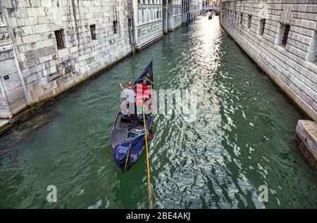 Gondoliere auf einer Gondel in einem Kanal im Gespräch mit Touristen Passagiere; Venedig, Italien Stockfoto