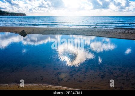 Sonne und Wolken spiegeln sich in den flachen Pools am Strand bei Ebbe Stockfoto