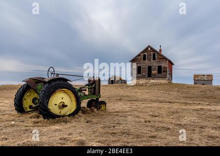 Altes verlassene Bauernhaus auf einem Hügel mit Blick auf einen Vintage-Traktor auf einer Weide auf den Prärien in Saskatchewan Stockfoto
