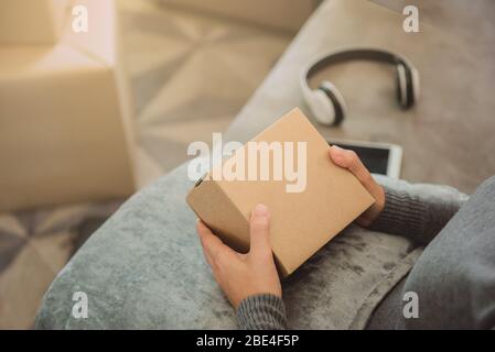Frau, die ein Paket hält, das von einem Online-Kauf auf einem Sofa mit Telefon und Kopfhörer erhalten wurde. Online-Shopping. Geschäft Online-Verkäufer.mit Kopierraum Stockfoto