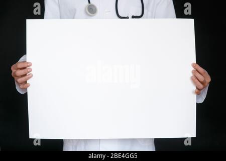 Ein Mann in einem schwarzen T-Shirt und medizinischen Handschuhen hält ein weißes Blatt Papier. Modell. Coronavirus. Quarantäne . Epidemie. Kopierbereich. Warnung. Arzthand in blauem Handschuh mit Papierblättern. Stockfoto