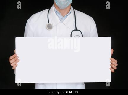 Ein Mann in einem schwarzen T-Shirt und medizinischen Handschuhen hält ein weißes Blatt Papier. Modell. Coronavirus. Quarantäne . Epidemie. Kopierbereich. Warnung. Arzthand in blauem Handschuh mit Papierblättern. Stockfoto