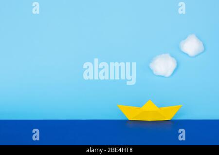 Gelbes Papierboot, das sich auf blauem Meer mit Himmel und Wolken bewegt. Minimales Reise- und Urlaubskonzept. Stockfoto