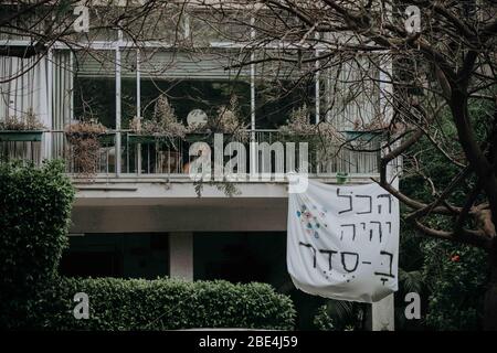 Ein selbstgemachter Schild hängt von einem Balkon, der sagt: "Alles wird in Ordnung sein" auf Hebräisch als Selbsthilfe für andere während der COVID-19 Quarantäne. Fotofotografie Stockfoto