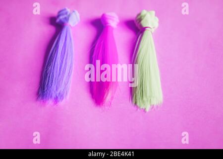 Mehrfarbige gerade lange Haare, Perücken für handgefertigte Puppen auf rosa Hintergrund. Farbige Haarsträhnen. Handarbeit, Hobby, Freizeitkonzept. Draufsicht. Stockfoto