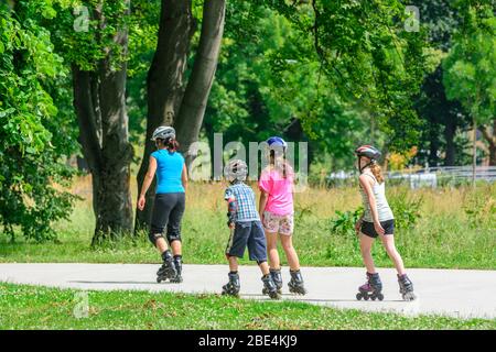 Junge Familie eine Tour auf Inlineskates im städtischen Park an einem sonnigen Mittag im Sommer Stockfoto