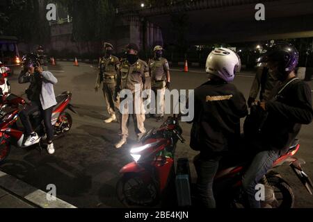 Jakarta, Indonesien. April 2020. Beamte untersuchen Motorradfahrer während der Umsetzung der umfassenden sozialen Einschränkung im Rahmen der COVID-19-Pandemie in Jakarta, Indonesien am 11. April 2020. Der indonesische Präsident Joko Widodo hat den Ausbruch als Notstand für die öffentliche Gesundheit erklärt und eine staatliche Verordnung über umfangreiche soziale Beschränkungen erlassen. Kredit: Aditya Irawan/Xinhua/Alamy Live News Stockfoto