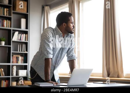 Nachdenklicher afroamerikanischer Geschäftsmann, der sich auf den Tisch gelehnt und wegschaut. Stockfoto