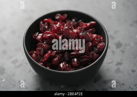 Getrocknete Preiselbeeren in schwarzer Schale auf Betonoberfläche Stockfoto