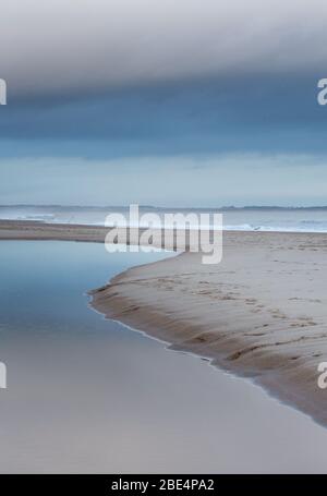 Die gekrümmte Linie eines Baches, der über den Sand fließt und in die Druridge Bay, Northumberland im Nordosten Englands, führt. Stockfoto