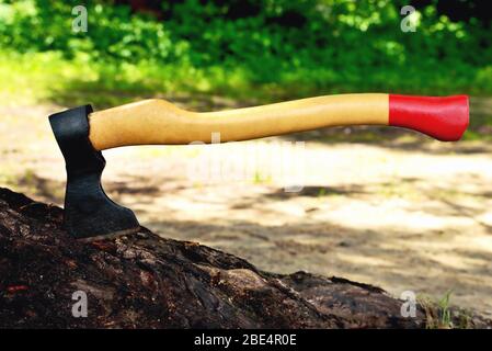 Eine schöne Axt ragt in einem Baum hervor, mit einem gelben Griff aus der Nähe, auf einem natürlichen Hintergrund Stockfoto