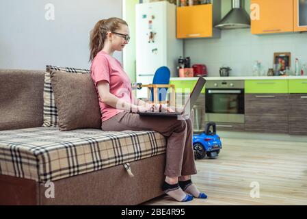 Eine junge Frau arbeitet ferngesteuert an einem Laptop. Das Konzept der Fernarbeit und Online-Bildung. Nützlicher Zeitvertreib, wenn man zu Hause bleiben muss. Stockfoto
