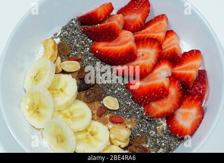 Schüssel voll Joghurt mit Erdbeeren, Bananenscheiben, Chiasamen, Nüssen, Goji-Beeren und Rosinen bedeckt. Konzept : nahrhaftes Frühstück. Stockfoto