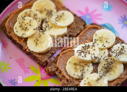 Scheiben von gesunden Brot mit Erdnussbutter verteilen Bananenscheiben und Chiasamen auf einem Teller für Mädchen. Konzept: Gesunde Ernährungsgewohnheiten für Kinder. Stockfoto