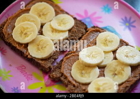 Scheiben von gesunden Brot mit Erdnussbutter und Bananenscheiben auf einem Teller für Mädchen. Konzept: Gesunde Ernährungsgewohnheiten für Kinder. Stockfoto