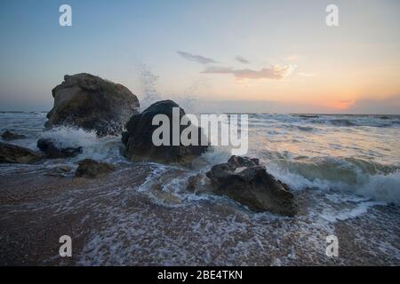 Bei Sonnenuntergang schlagen sich spritzende Wellen gegen die Felsen am Strand. Krim Stockfoto