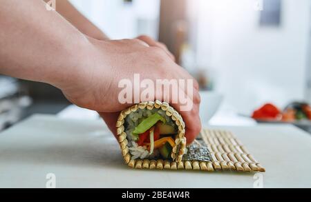 Prozess der Roll-up Sushi-Rolle mit Gemüse mit Bambus-Matte, von der Seite in Nahaufnahme gesehen Stockfoto