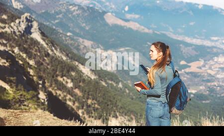 Tourist Mädchen, die ein Fotoshooting von Berg machen. Das junge, schöne Mädchen reist allein im Frühjahr oder Herbst in die Berge, blickt in die Ferne und genießt Natur, Felsen und grüne Wälder, Blick auf die Landschaft. Ein Rucksack dahinter und Sportswear, Freiheit und Leichtigkeit, verloren gegangen und auf der Suche nach Koordinaten Stockfoto