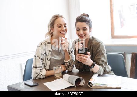 Zwei glückliche junge Frauen Freunde im Cafe sitzen, Kaffee, an Handy suchen Stockfoto