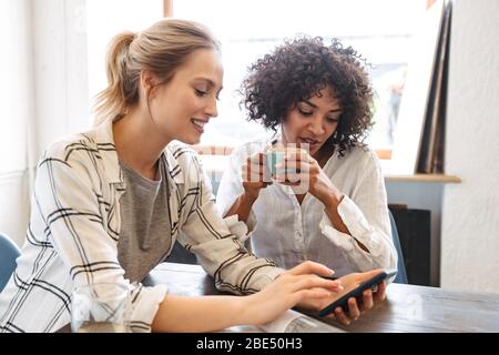 Zwei glückliche junge Frauen Freunde im Cafe sitzen, Kaffee, mit Handy Stockfoto
