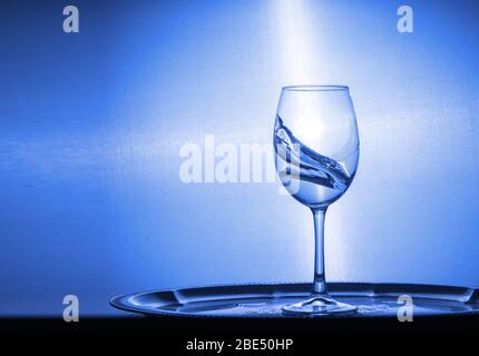 Kaltes transparentes Wasser spritßt aus einem Glas, das auf dem Holztisch in der Nähe bleibt Stockfoto