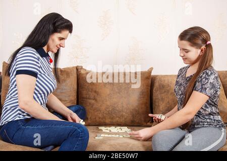 Mutter und Tochter spielen Dominosteine, während sie zu Hause auf einem Sofa sitzen. Coronavirus Quarantäne Stockfoto