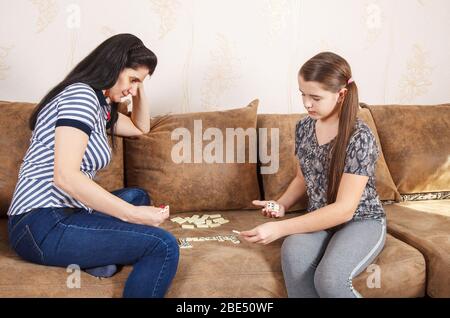 Mutter und Tochter spielen Dominosteine, während sie zu Hause auf einem Sofa sitzen. Coronavirus Quarantäne Stockfoto