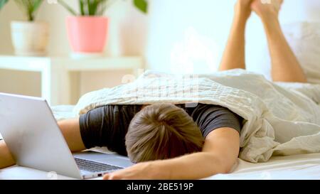 Ein Mann arbeitet im Schlafzimmer an einem Laptop zu Hause. Konzept für die Fernarbeit zu Hause während der Coronavirus Quarantäneperiode Covid 19. Stockfoto