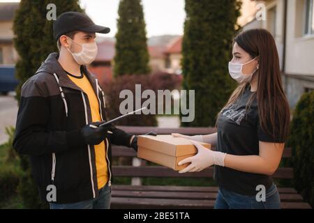 Mann vom Lieferservice in medizinischer Maske und Handschuhen, der frische Lebensmittel an junge Frau weitergibt, die Express-Lieferung vom Kurier zu Hause erhält Stockfoto