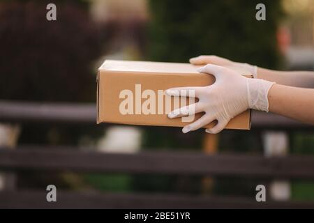 Nahaufnahme Hände in Schutzhandschuhe Paket halten. Lieferung dervise bringen Ordnung an den Kunden. Online-Shopping-Konzept. Schwarze und weiße Handschuhe Stockfoto
