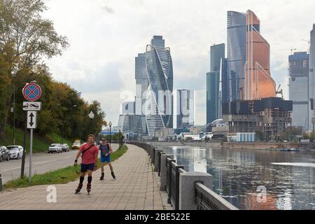 Moskau, Russland, 21. August 2019: Zwei junge Jungs Rollen auf der Promenade vor der Kulisse von Wolkenkratzern Stockfoto