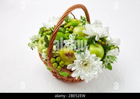 Weidenkorb mit Früchten, weißen und grünen Blüten auf weißem Hintergrund gefüllt Stockfoto