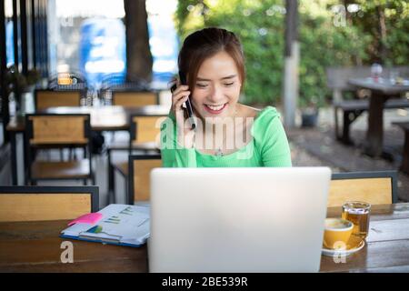 Asiatische Business-Frauen nutzen Handy und Touch-Smartphone für Kommunikation und Frauen mit Notebook für die Arbeit Stockfoto