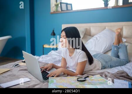 Junge Frau im Bett liegend mit gekreuzten Beinen, tippen auf Laptop Stockfoto