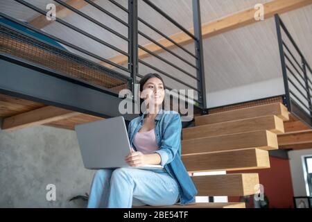 Junge Frau auf Treppen sitzend, Laptop auf Knien haltend, seitwärts schauend Stockfoto