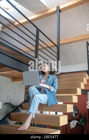 Junge Frau auf Treppen sitzend, Laptop auf Knien haltend, tippend Stockfoto