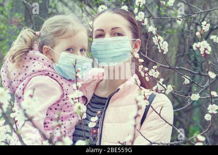 Porträt einer Mutter und Tochter in Masken auf der Straße in der Nähe eines blühenden Baumes. Stockfoto