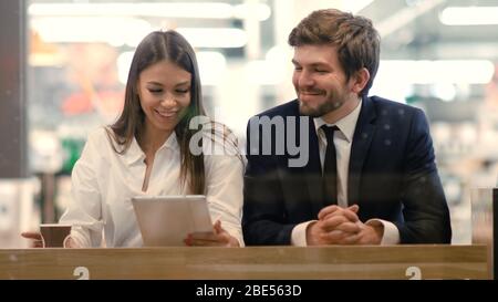 Geschäftsmann und -Frau sitzen mit Tablet in einem Einkaufszentrum. Stockfoto