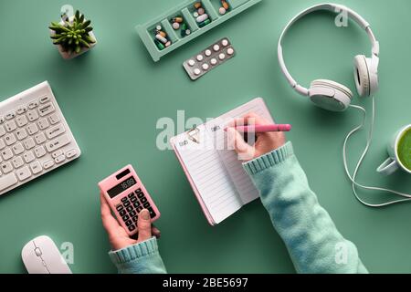 Kreatives, flaches Design mit Notebook zur Überwachung der Medikamentenkosten. Hände mit Stift und Taschenrechner. Verschiedene Pillen und Pille Fall auf grünem Minze Hintergrund. Überwachung Stockfoto