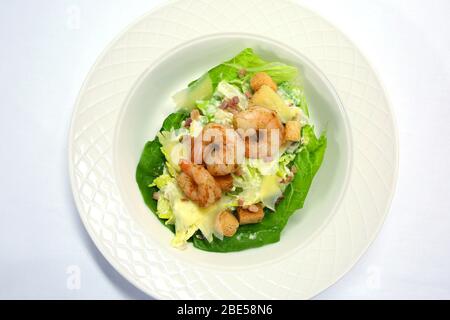 Ceaser Salat mit Garnelen, die zum Essen zubereitet werden, serviert auf einem weißen porzellanplatte auf einem weißen Tischtuch. Stockfoto