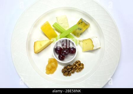 Eine Auswahl an Käse mit Trauben, Chutney, Sellerie und Walnüssen, die alle als Käseplatte auf einem weißen Tischtuch zubereitet werden. Stockfoto