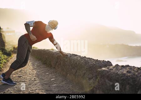 Senior fit Mann Stretching Outdoor bei Sonnenuntergang vor dem Workout-Session - Reifen Sportler Training draußen, während Playlist Musik hören - Sport und freudig Stockfoto